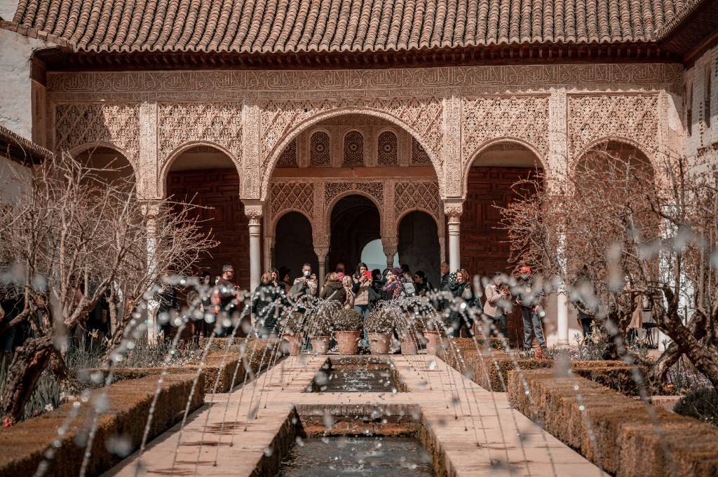 A Granada courtyard with a long reflecting pool, carved Nasrid arches and visitors under the façade.